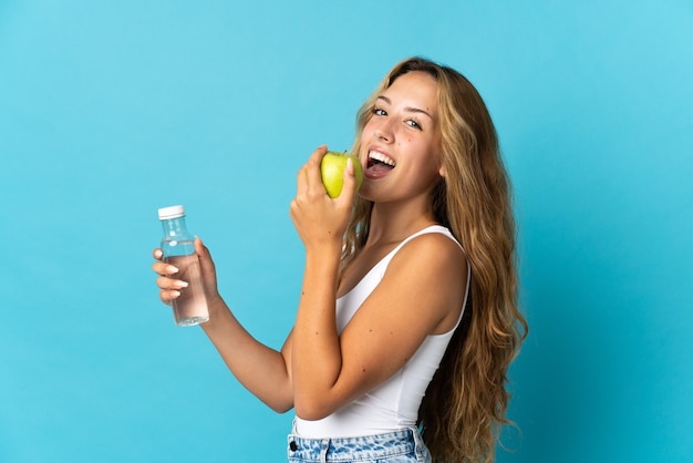 Jeune femme blonde isolée avec une pomme et avec une bouteille d'eau