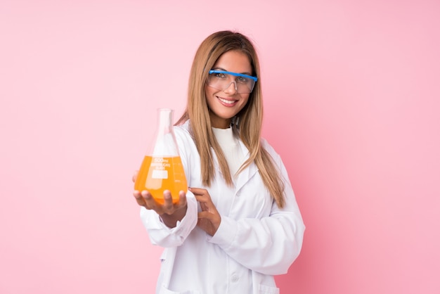 Jeune femme blonde isolée sur rose avec un tube à essai scientifique