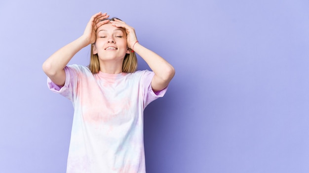 Jeune femme blonde isolée sur violet rit joyeusement en gardant les mains sur la tête. Concept de bonheur.