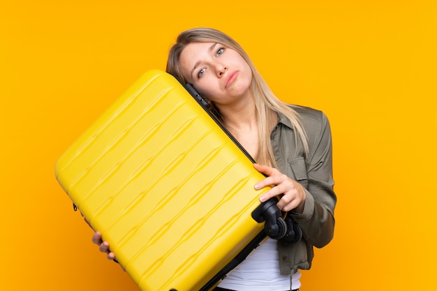 Jeune femme blonde sur jaune en vacances avec valise de voyage et malheureux