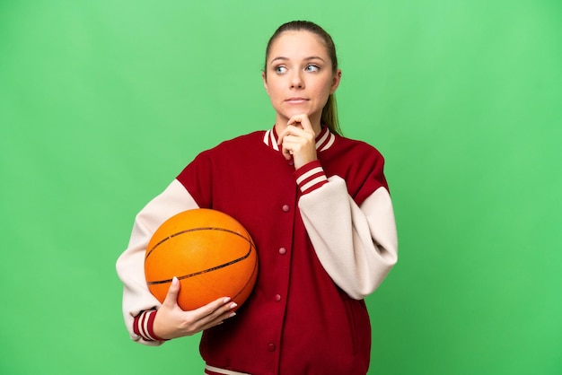 Jeune femme blonde jouant au basket-ball sur fond isolé chroma key ayant des doutes et pensant