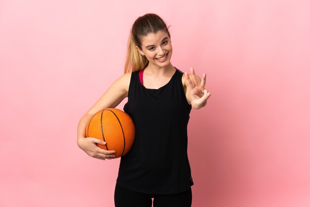 Jeune femme blonde jouant au basket isolé sur fond rose heureux et en comptant trois avec les doigts