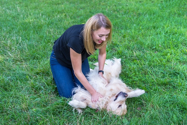 Jeune femme blonde jouant avec un chien golden retriever dans le parc