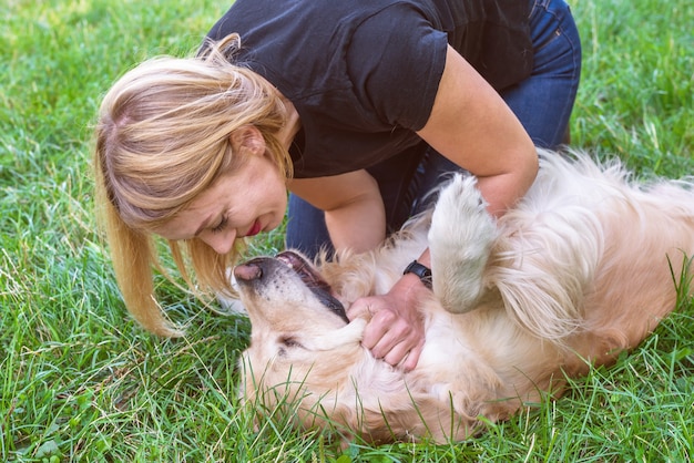 Jeune femme blonde jouant avec un chien golden retriever dans le parc