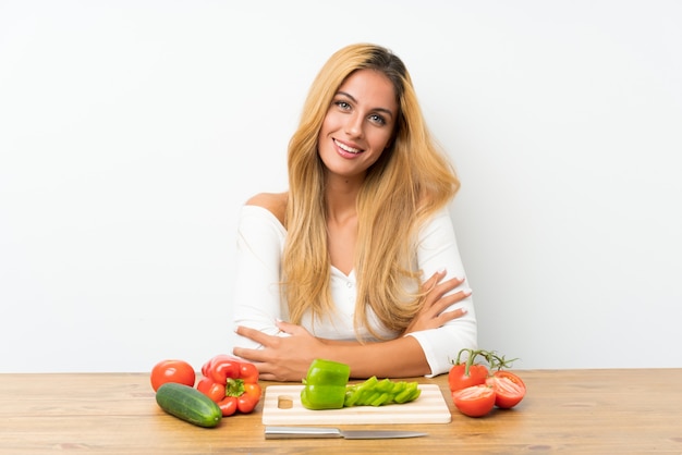 Jeune femme blonde avec des légumes dans une table en riant