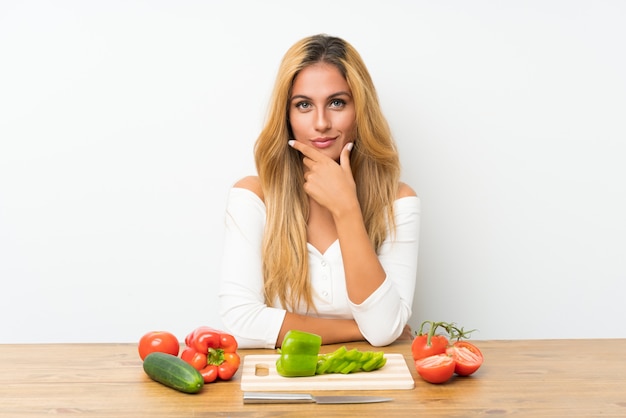 Jeune femme blonde avec des légumes dans une table en riant