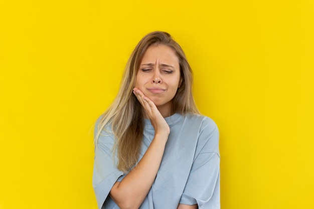 Une jeune femme blonde avec un mal de dents tenant sa joue isolée sur fond jaune de couleur