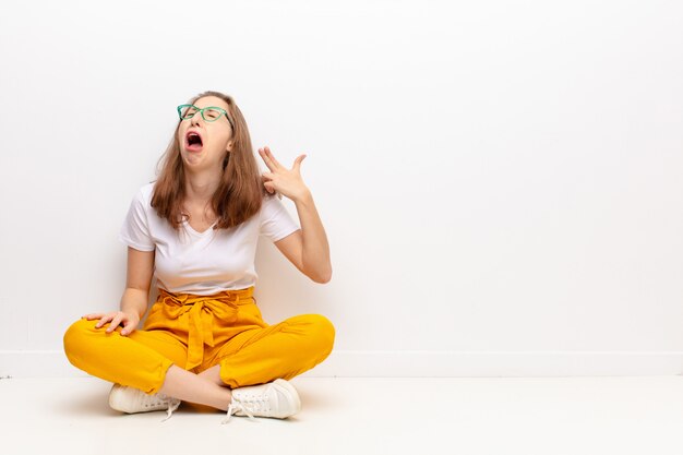 Jeune femme blonde à la malheureuse et stressée, geste de suicide faisant signe du pistolet avec la main, pointant vers la tête assise sur le sol