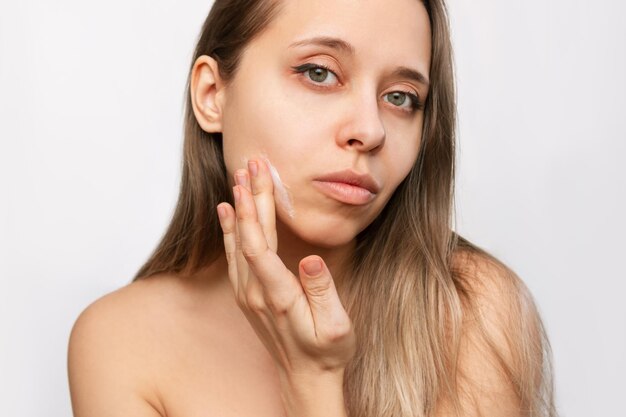 Une jeune femme blonde maquillée touchant le visage avec sa main appliquant une crème hydratante