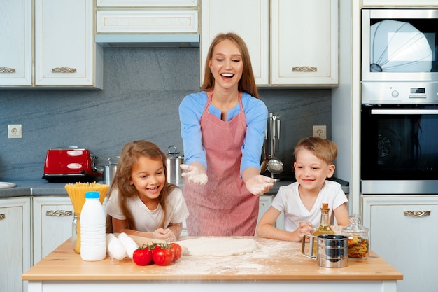 Jeune femme blonde, mère et ses enfants s'amusant pendant la cuisson de la pâte se bouchent