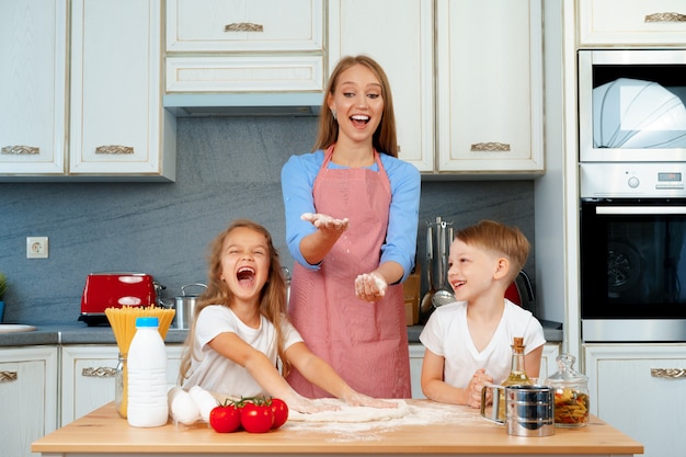 Jeune femme blonde, mère et ses enfants s'amusant pendant la cuisson de la pâte