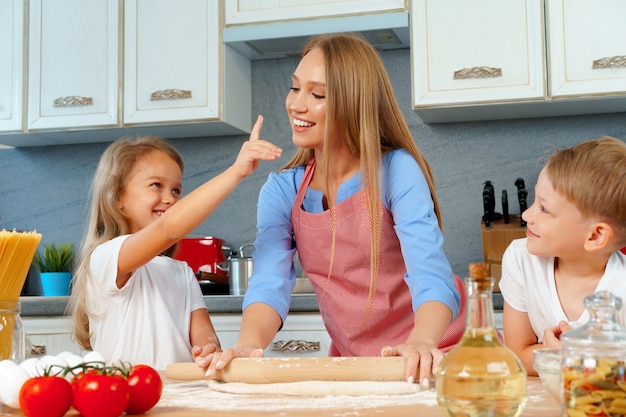 Jeune femme blonde, mère et ses enfants s'amusant pendant la cuisson de la pâte