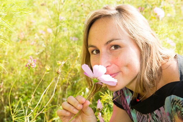 Jeune femme blonde mignonne sentant des fleurs roses