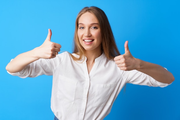 Jeune femme blonde montrant les pouces vers le haut signe sur fond bleu