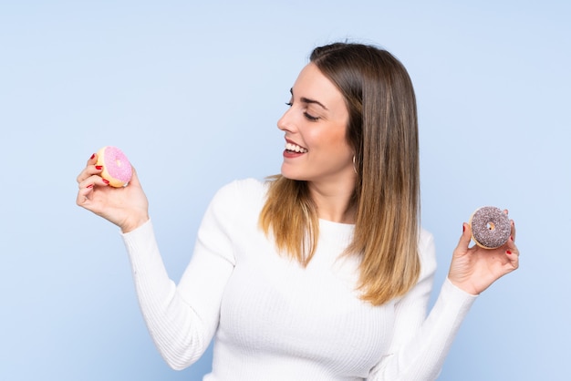 Jeune femme blonde sur un mur bleu isolé tenant des beignets avec une expression heureuse