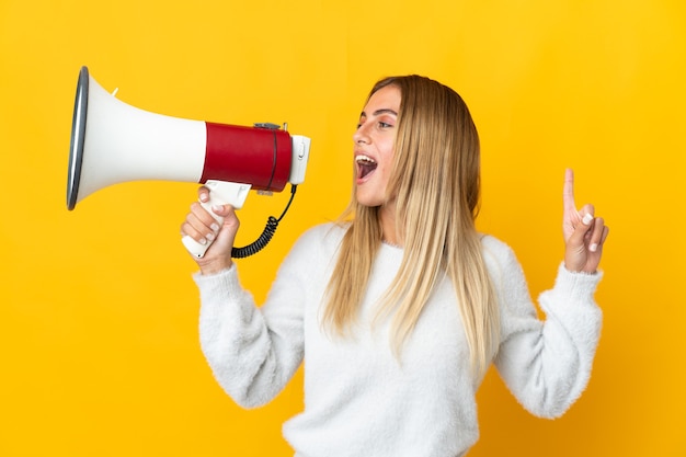 Jeune femme blonde sur mur isolé criant à travers un mégaphone pour annoncer quelque chose en position latérale