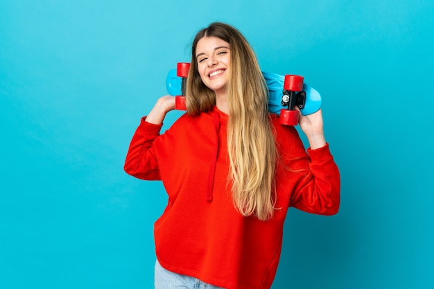 Jeune femme blonde sur un mur isolé avec un patin avec une expression heureuse