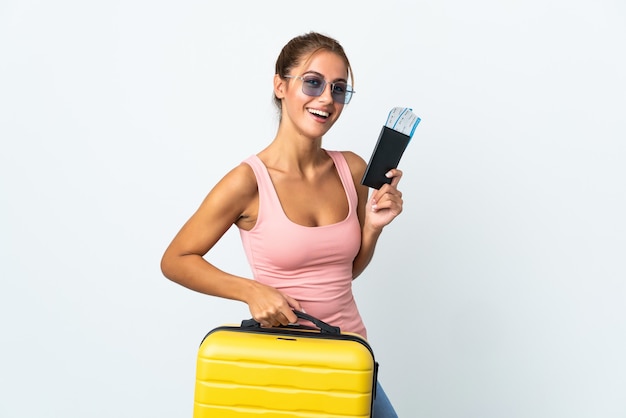 Jeune femme blonde sur mur isolé en vacances avec valise et passeport