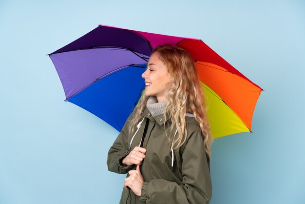 Jeune femme blonde avec un parapluie sur bleu avec une expression heureuse