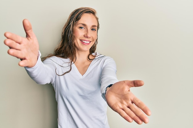 Jeune femme blonde portant des vêtements décontractés regardant la caméra en souriant à bras ouverts pour un câlin. expression joyeuse embrassant le bonheur.