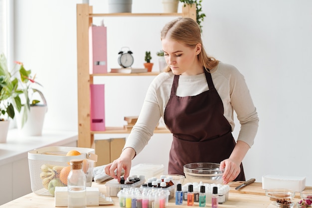 Jeune femme blonde prenant l'une des bouteilles d'huiles essentielles tout en choisissant le parfum du savon artisanal