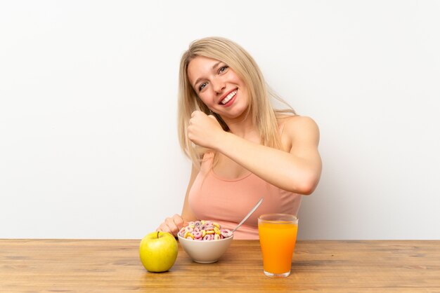 Jeune femme blonde prenant son petit déjeuner célébrant une victoire