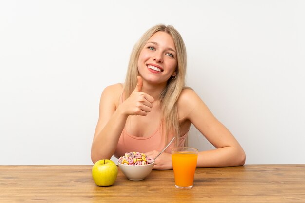 Jeune femme blonde prenant son petit déjeuner donnant un geste du pouce levé