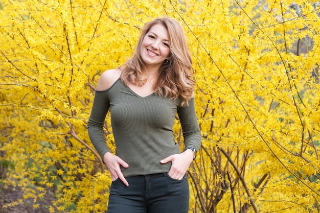 Jeune femme blonde près de la floraison des arbres jaunes dans le parc du printemps aux beaux jours.