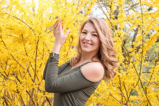 Jeune femme blonde près de la floraison des arbres jaunes dans le parc du printemps aux beaux jours.