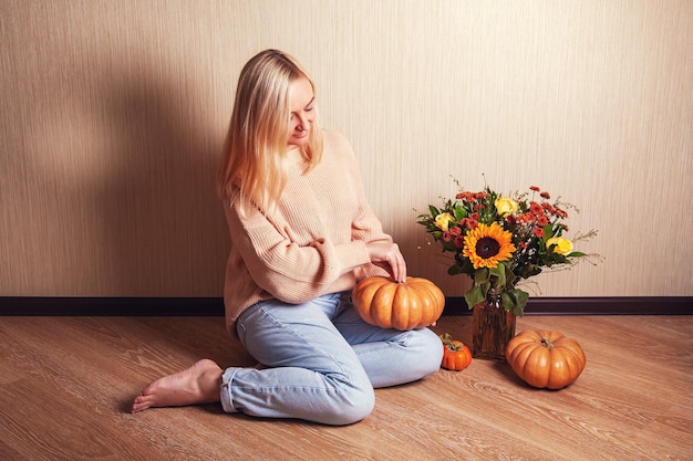 Jeune femme blonde en pull chaud est assise sur le sol et tient la citrouille dans ses mains et regarde-la