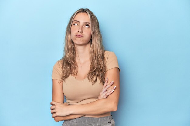 Jeune femme blonde de race blanche en studio bleu fatiguée d'une tâche répétitive