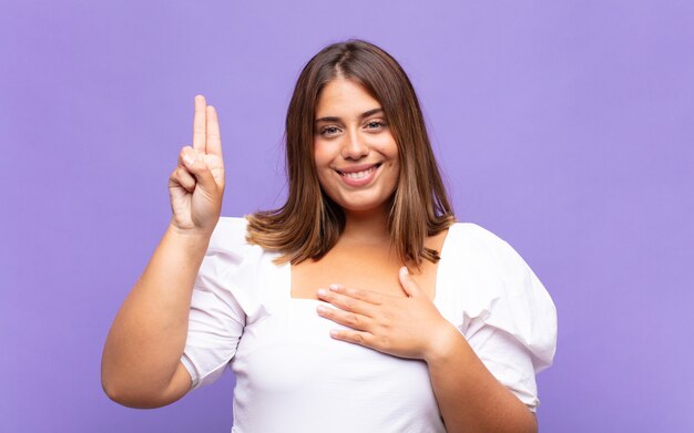 Jeune femme blonde à la recherche de bonheur, confiant et digne de confiance, souriant et montrant le signe de la victoire, avec une attitude positive