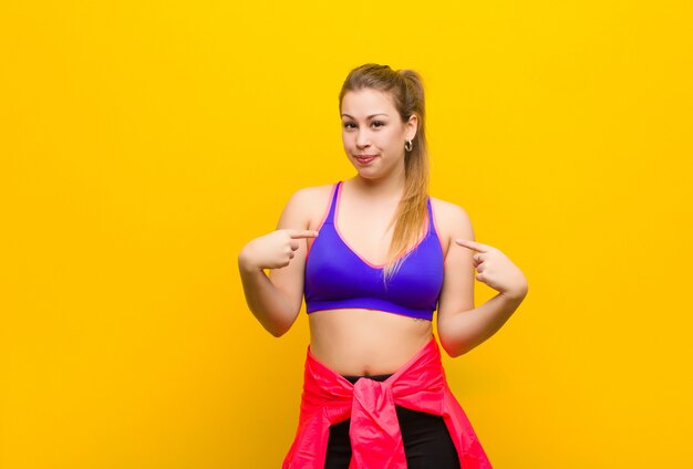 Jeune femme blonde à la recherche de fierté, positive et décontractée pointant vers la poitrine avec les deux mains. concept de sport