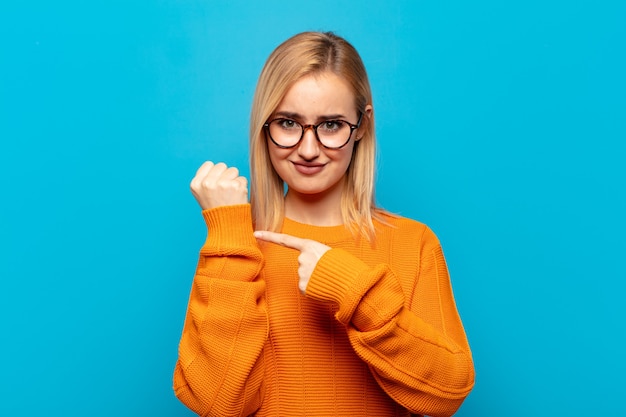 Jeune femme blonde à la recherche d'impatience et en colère, pointant sur la montre, demandant la ponctualité, veut être à l'heure