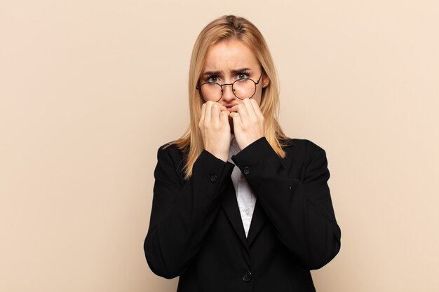 Jeune femme blonde à la recherche de soucis, anxieux, stressés et effrayés, se ronger les ongles et à la recherche de l'espace de copie latérale