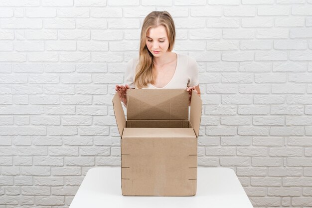 Jeune femme blonde regardant dans une boîte avec un fond de briques blanches