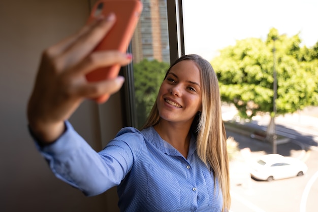 jeune femme blonde regardant par la fenêtre tout en prenant un café et en passant un appel vidéo