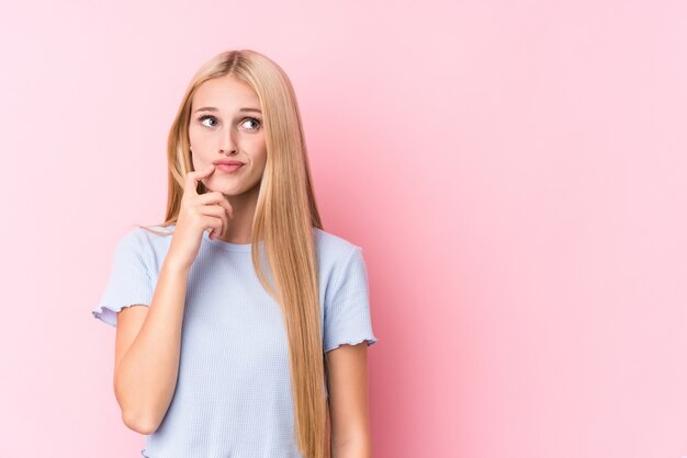 Jeune femme blonde en rose regardant sur le côté avec une expression douteuse et sceptique.