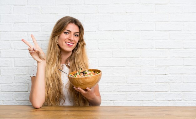 Jeune femme blonde avec une salade en geste de victoire