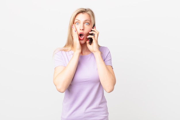 Jeune femme blonde se sentant choquée et effrayée et appelant avec un téléphone intelligent