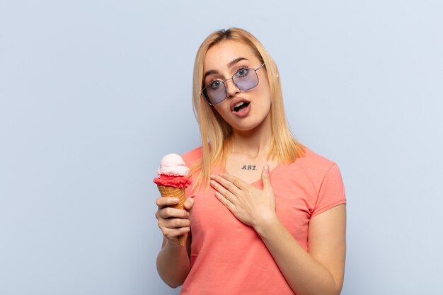 Jeune femme blonde se sentant choquée et surprise, souriante, prenant la main à cœur, heureuse d'être celle ou montrant sa gratitude