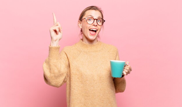 Jeune femme blonde se sentant comme un génie heureux et excité après avoir réalisé une idée, levant joyeusement le doigt, eurêka !. concept de café