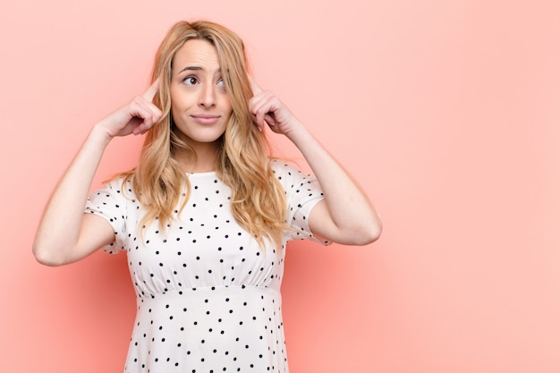 Photo jeune femme blonde se sentant confus ou doutant, se concentrant sur une idée, réfléchissant bien, à la recherche d'espace de copie sur le côté sur le mur de couleur plat