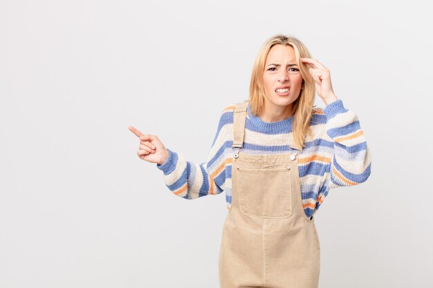 Jeune femme blonde se sentant confuse et perplexe, vous montrant que vous êtes fou