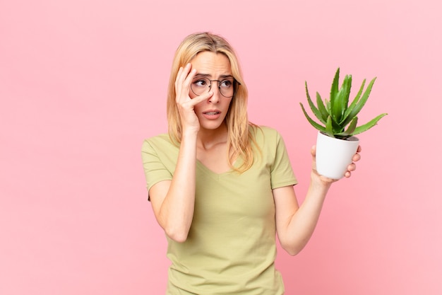 Jeune femme blonde se sentant ennuyée, frustrée et endormie après une fatigue et tenant un cactus