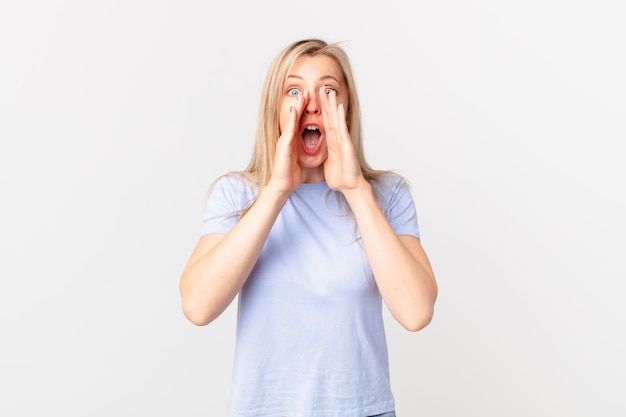 Jeune femme blonde se sentant heureuse, donnant un grand cri avec les mains à côté de la bouche