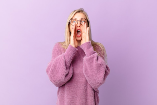 Jeune femme blonde se sentant heureuse, donnant un grand cri avec les mains à côté de la bouche