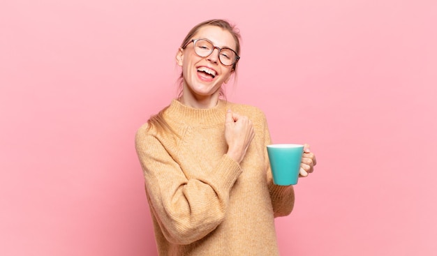 Jeune femme blonde se sentant heureuse, positive et réussie, motivée face à un défi ou célébrant de bons résultats. concept de café