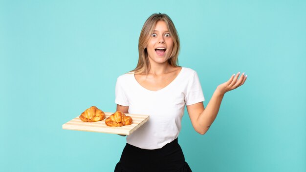 Photo jeune femme blonde se sentant heureuse, surprise de réaliser une solution ou une idée et tenant un plateau à croissants