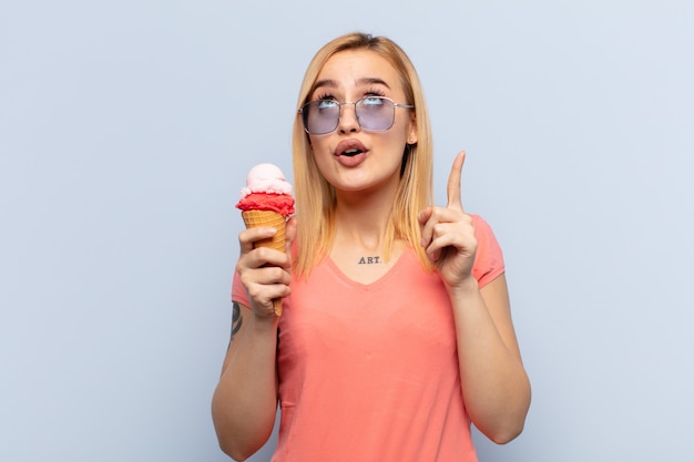 Jeune femme blonde se sentant impressionné et bouche ouverte pointant vers le haut avec un regard choqué et surpris